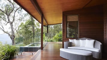 Una terraza de madera con un sofá y un jacuzzi con paredes de vidrio.