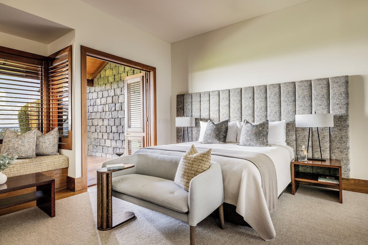 A modern bedroom with a large bed, a sofa, a nightstand, and a stone wall.