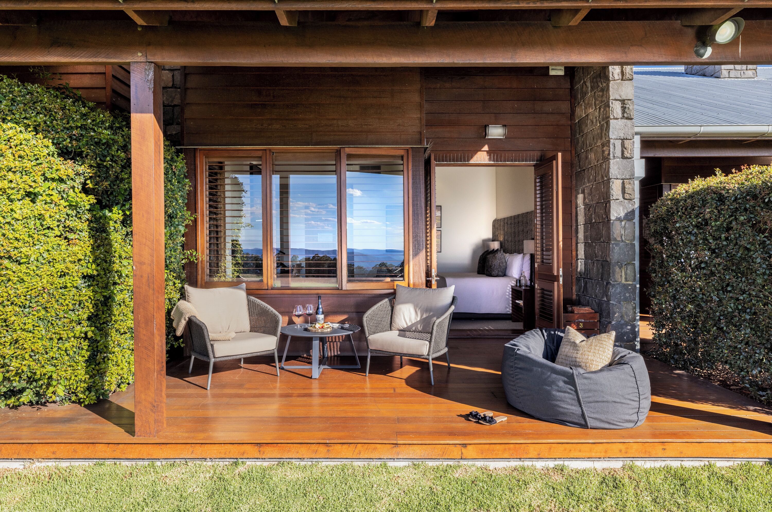 Una terraza de madera con mobiliario exterior, vistas al paisaje y un muro de piedra.