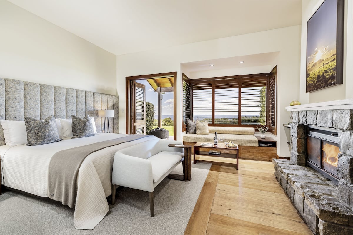 A modern bedroom with a large bed, a sofa, a fireplace, and a view of the outdoors.