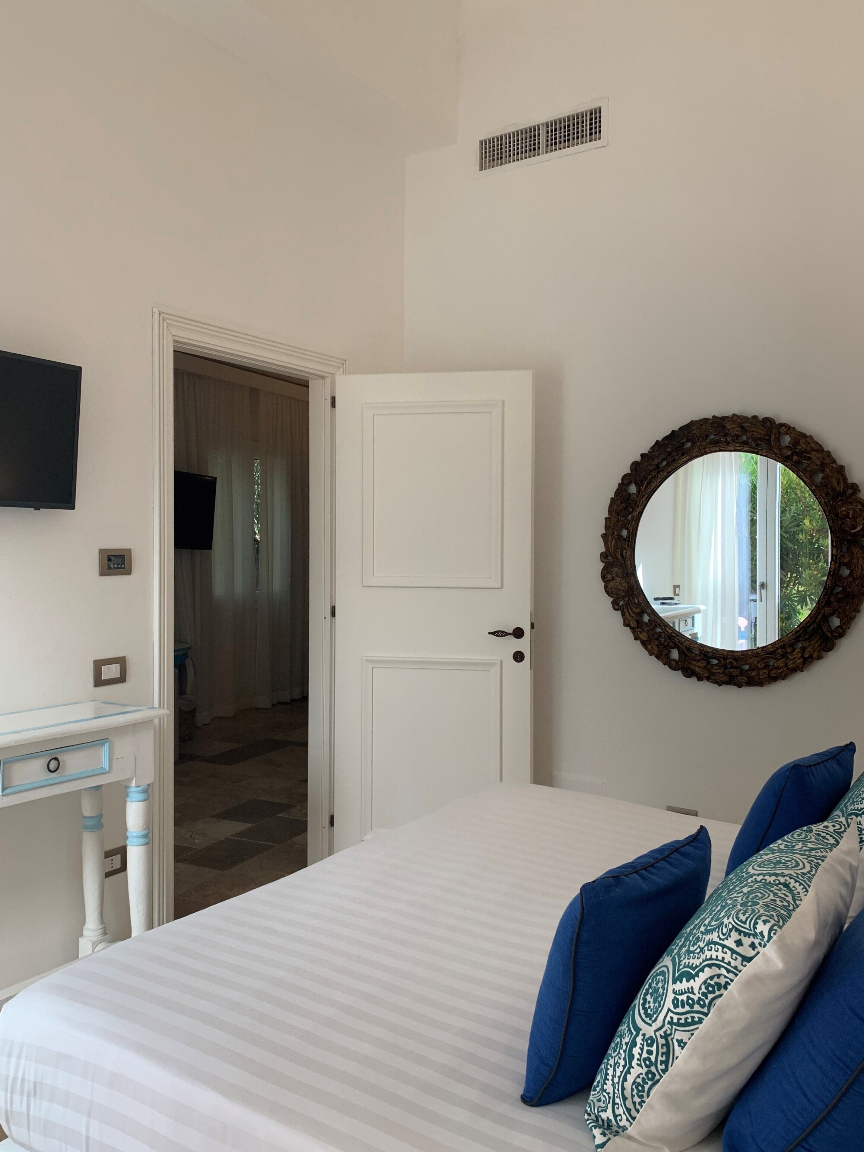 Un dormitorio con cama, cómoda, televisor, puerta y espejo.