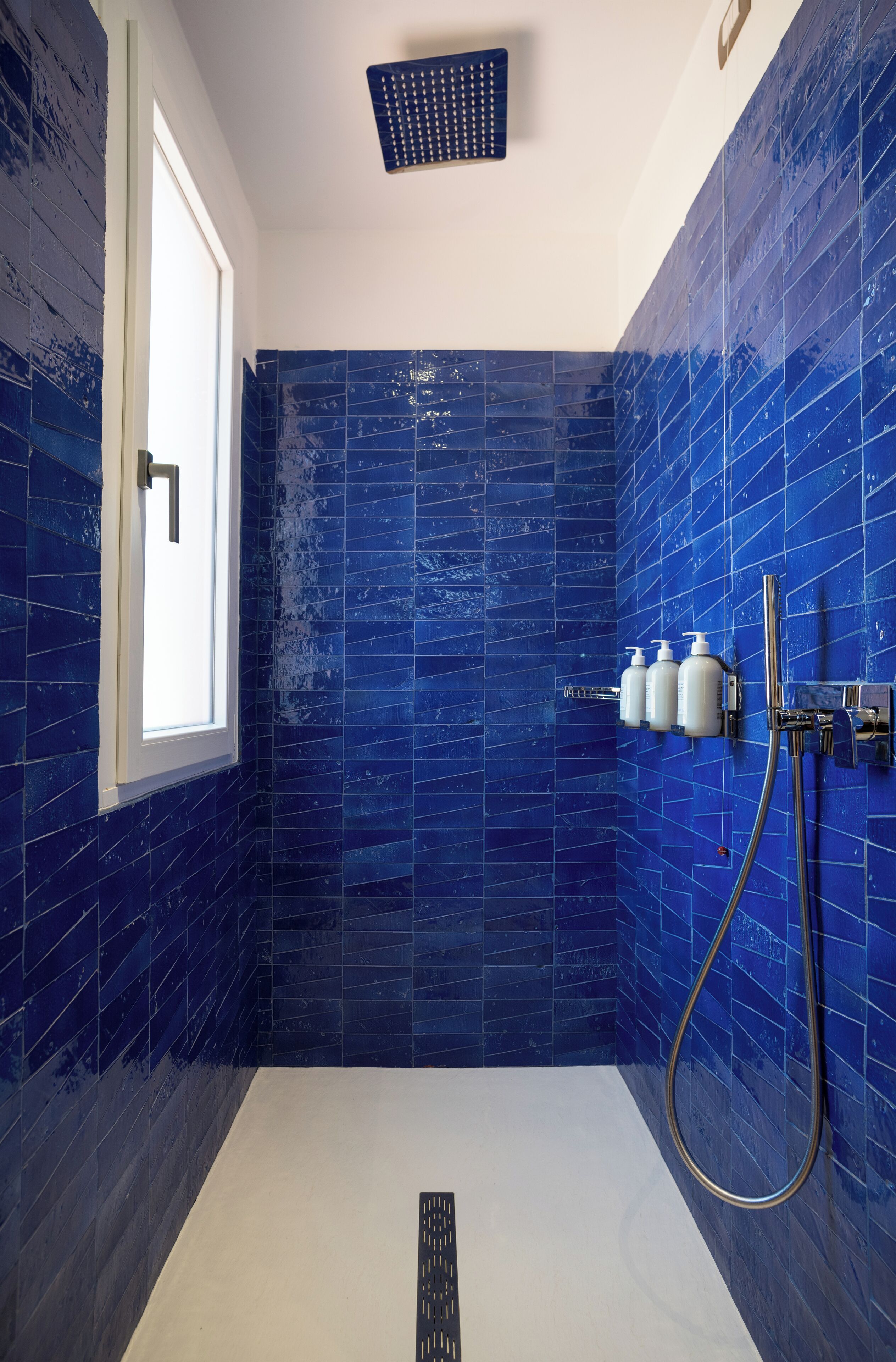 A bathroom with blue-tiled walls, a white bathtub, and a shower with a handheld showerhead.