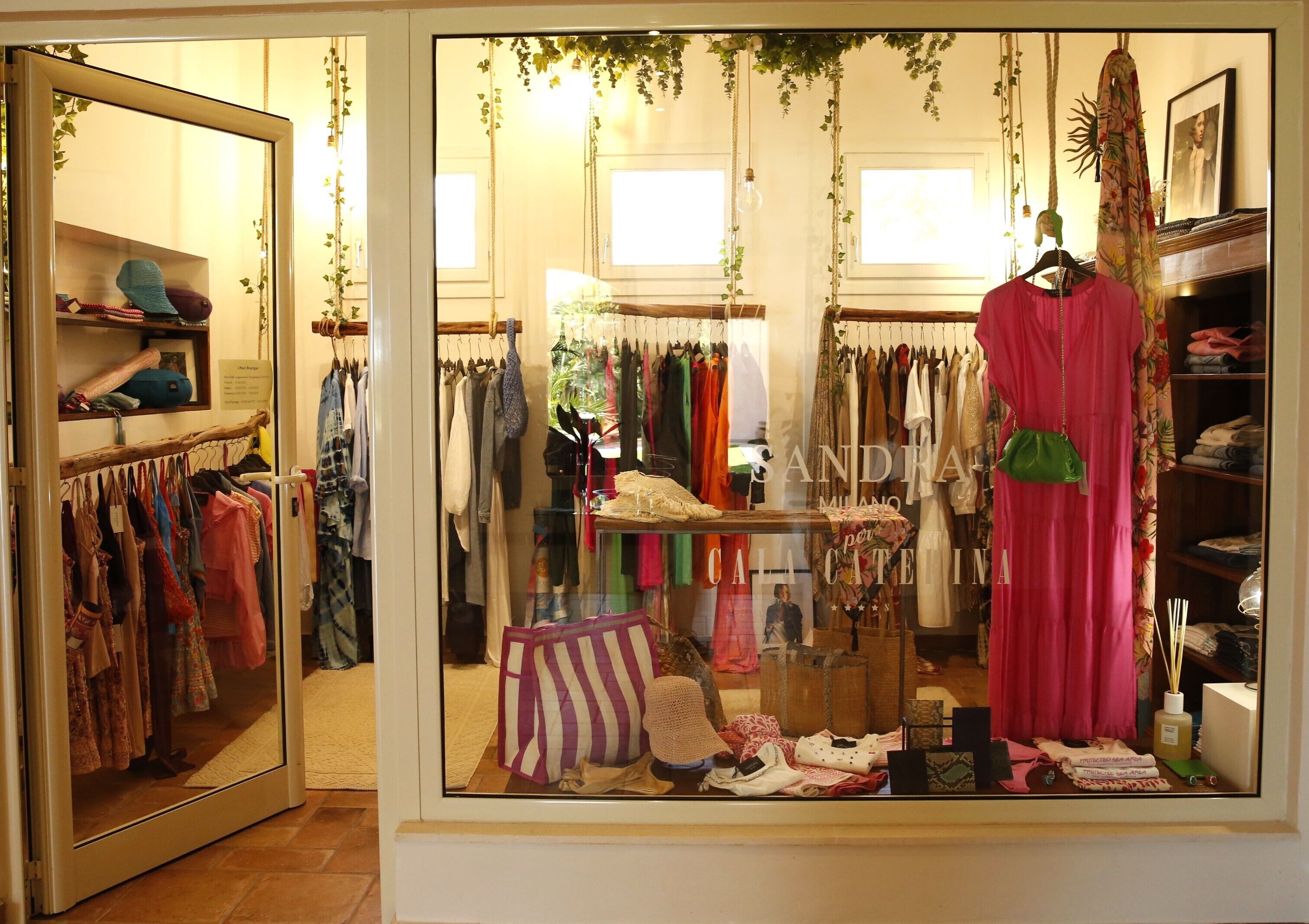 Une boutique de vêtements avec des portants remplis de vêtements, un présentoir de chapeaux et une robe rose suspendue à un cintre.