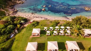 Vista aérea de un complejo turístico costero con sombrillas de playa, sillones reclinables y tiendas de campaña.