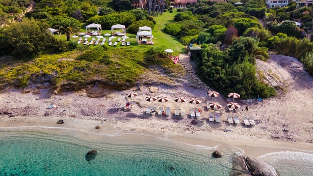 Vista aérea de una playa con aguas turquesas cristalinas, una orilla arenosa y varias sombrillas de playa.