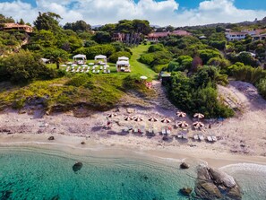 Vista aérea de una playa con aguas turquesas cristalinas, una orilla arenosa y varias sombrillas de playa.
