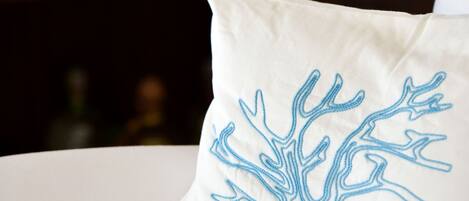 Almohada blanca con diseño de un árbol azul sobre un sofá blanco.
