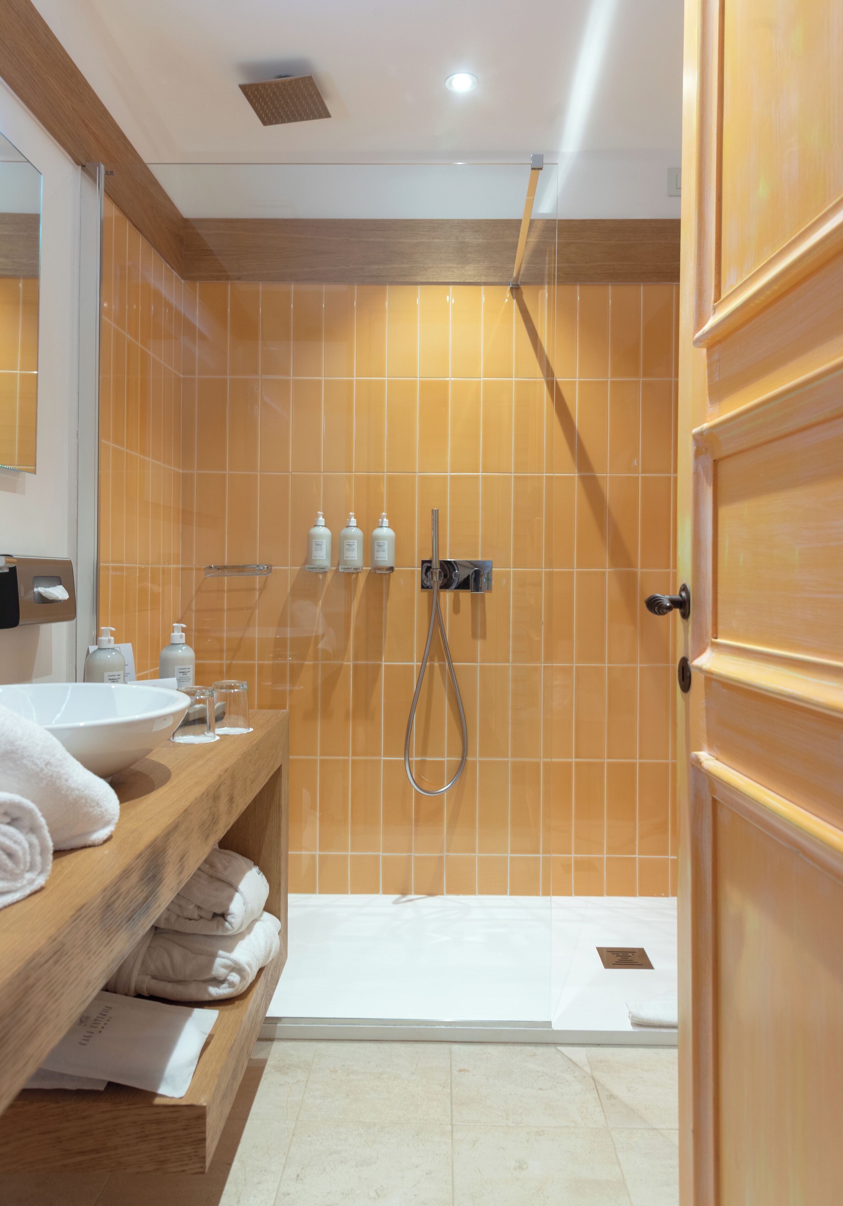 Een badkamer met een houten wastafelmeubel, een witte wasbak en een douche met een glazen deur.