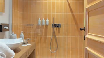 Een badkamer met een houten wastafelmeubel, een witte wasbak en een douche met een glazen deur.