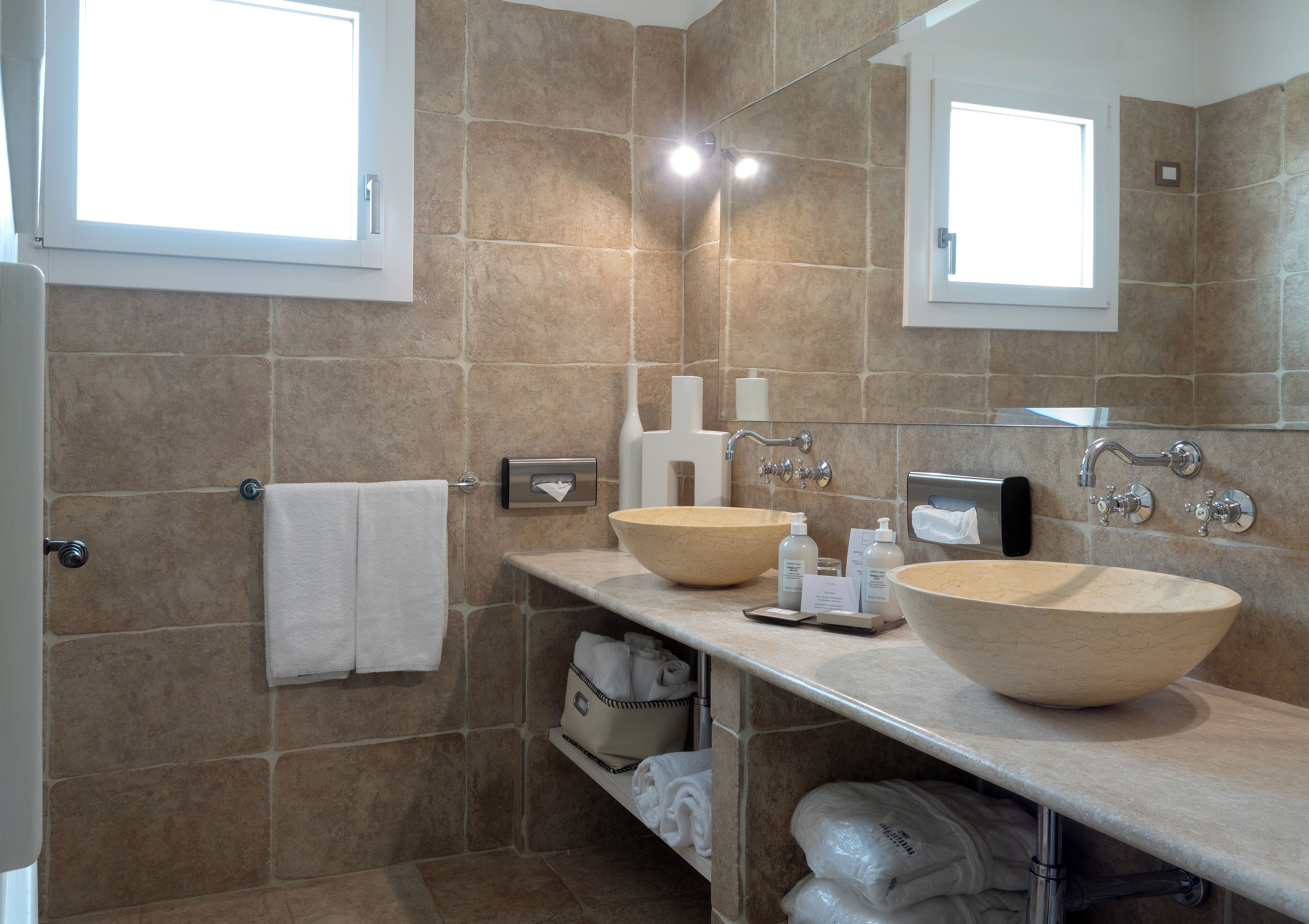 A modern bathroom with two large beige sinks, a mirror, and a towel rack.