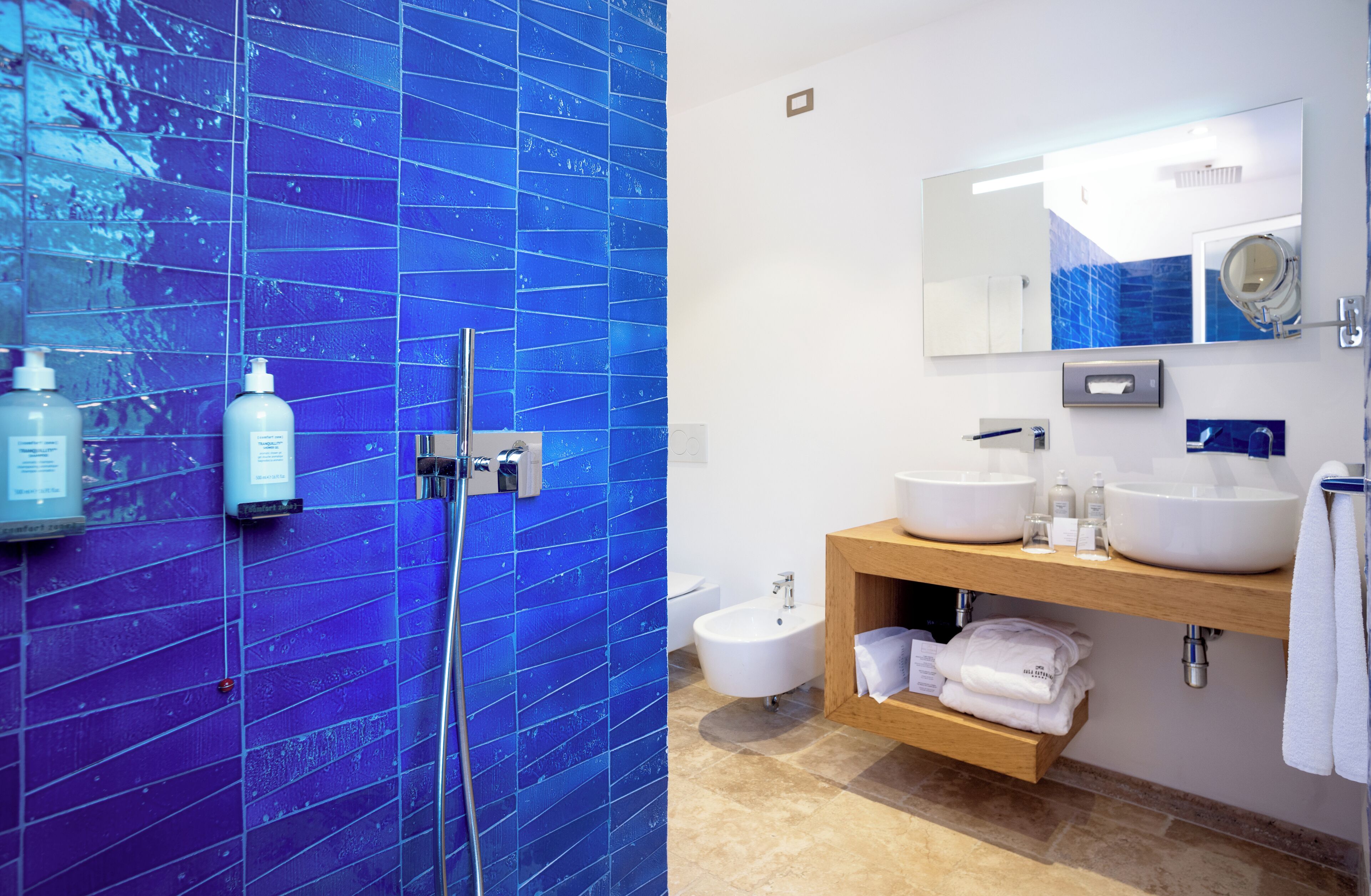 A bathroom with blue-tiled walls, a wooden vanity with two sinks, and a bidet.