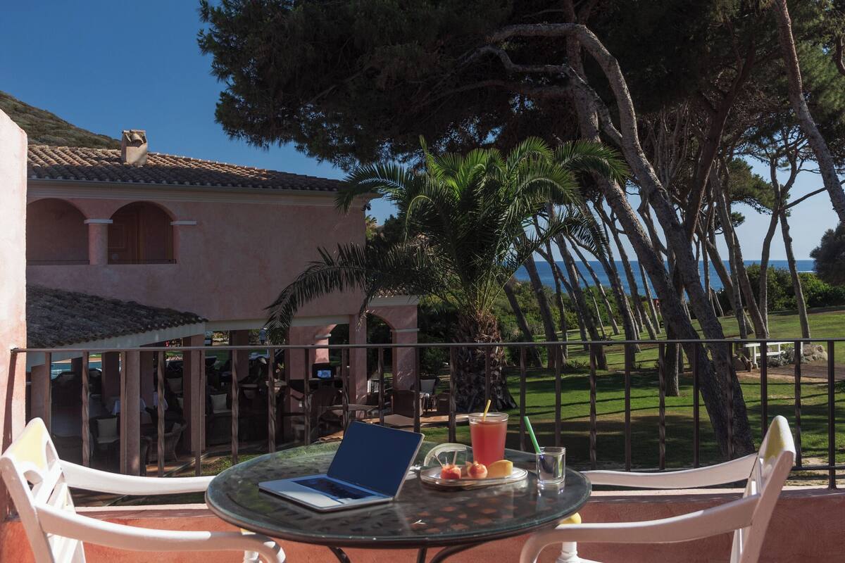 Een terras buiten met een ronde tafel, witte stoelen en een laptop.