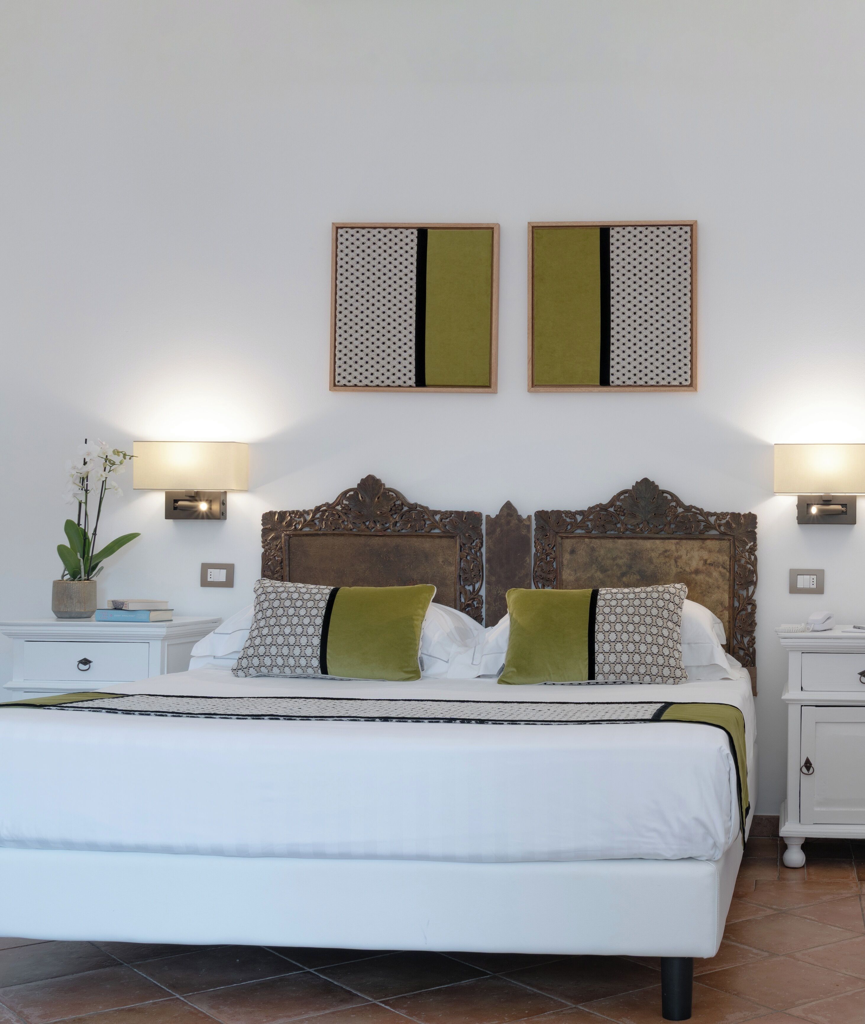 A neatly arranged bedroom with a large bed, two bedside tables, a decorative headboard, and two wall-mounted light fixtures.