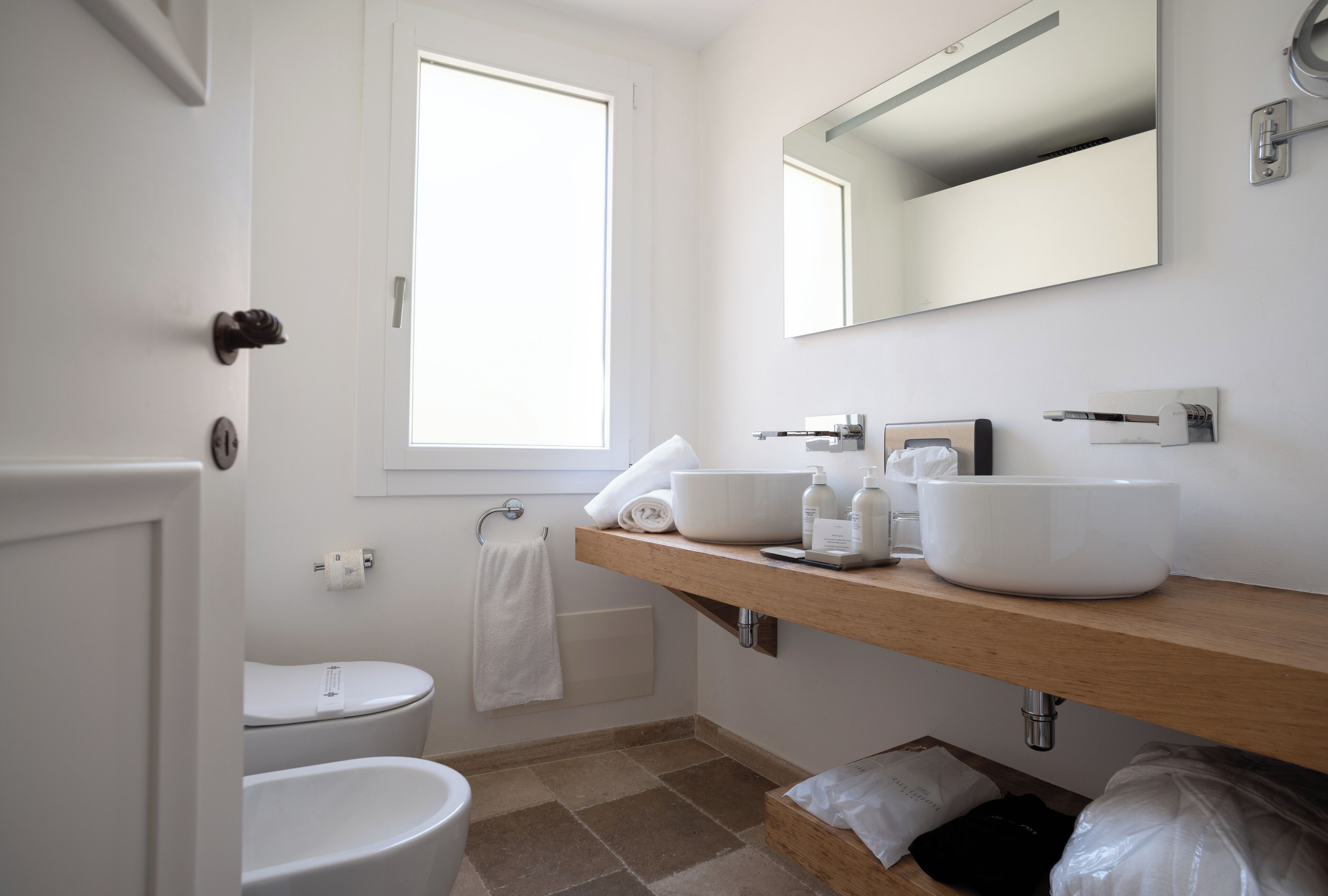 Un baño moderno con inodoro blanco, lavamanos con espejo y ventana que proporciona luz natural.
