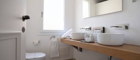 Un baño moderno con inodoro blanco, lavamanos con espejo y ventana que proporciona luz natural.
