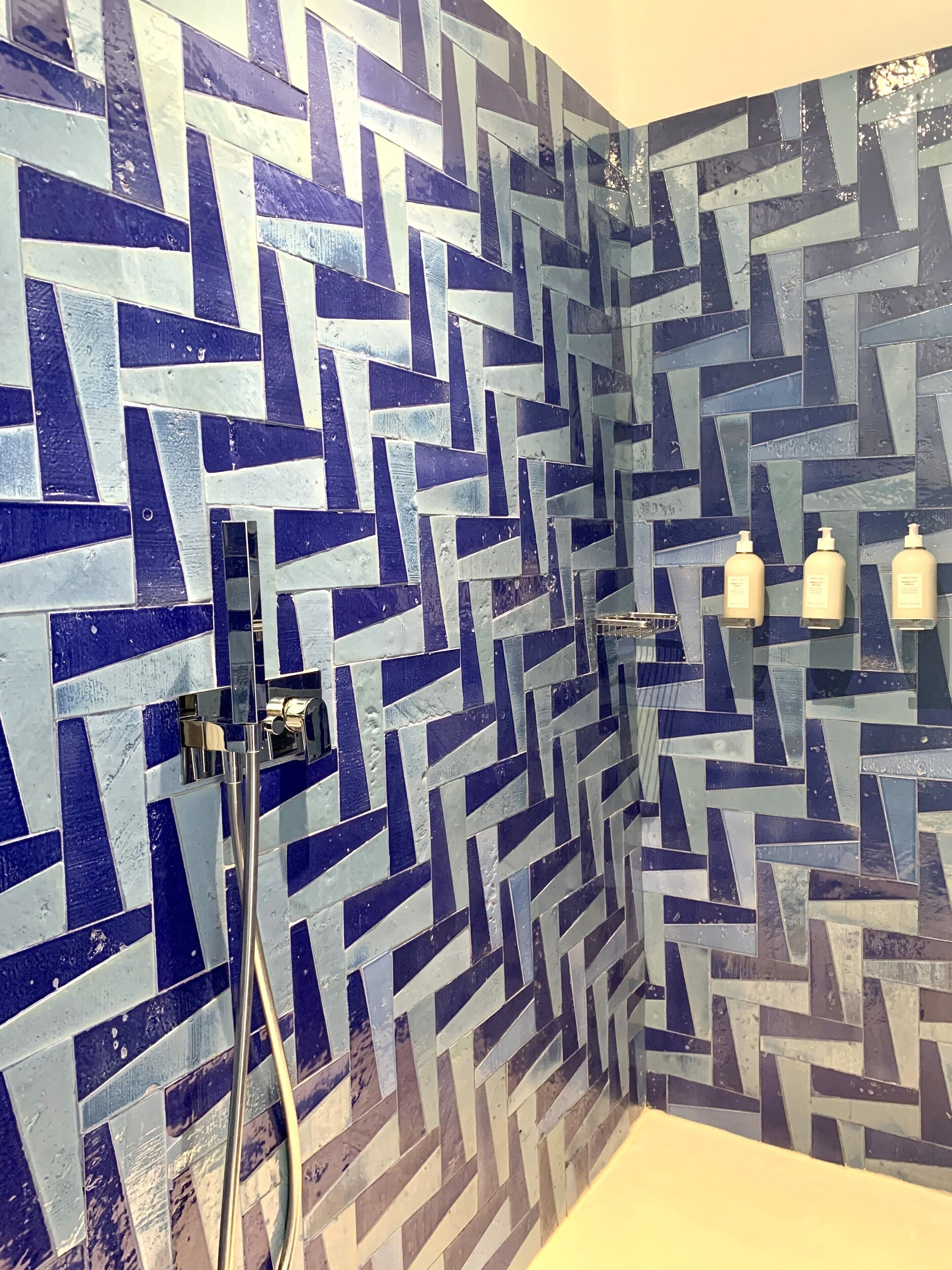 A bathroom with a geometric tile pattern on the walls, a shower area, and three bottles of toiletries on the wall.