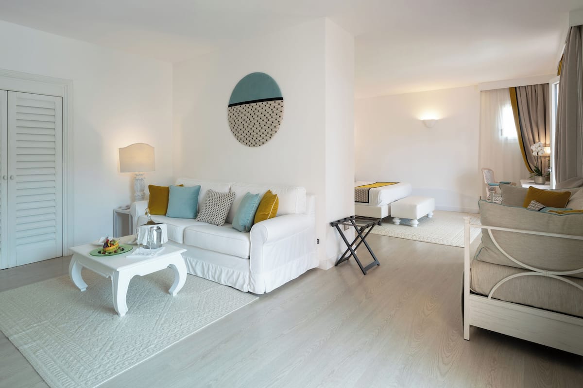 Een moderne woonkamer met een witte bank, een klein bijzettafeltje en een nachtkastje. Daarboven hangt een decoratief wandobject en op het nachtkastje staat een lamp.