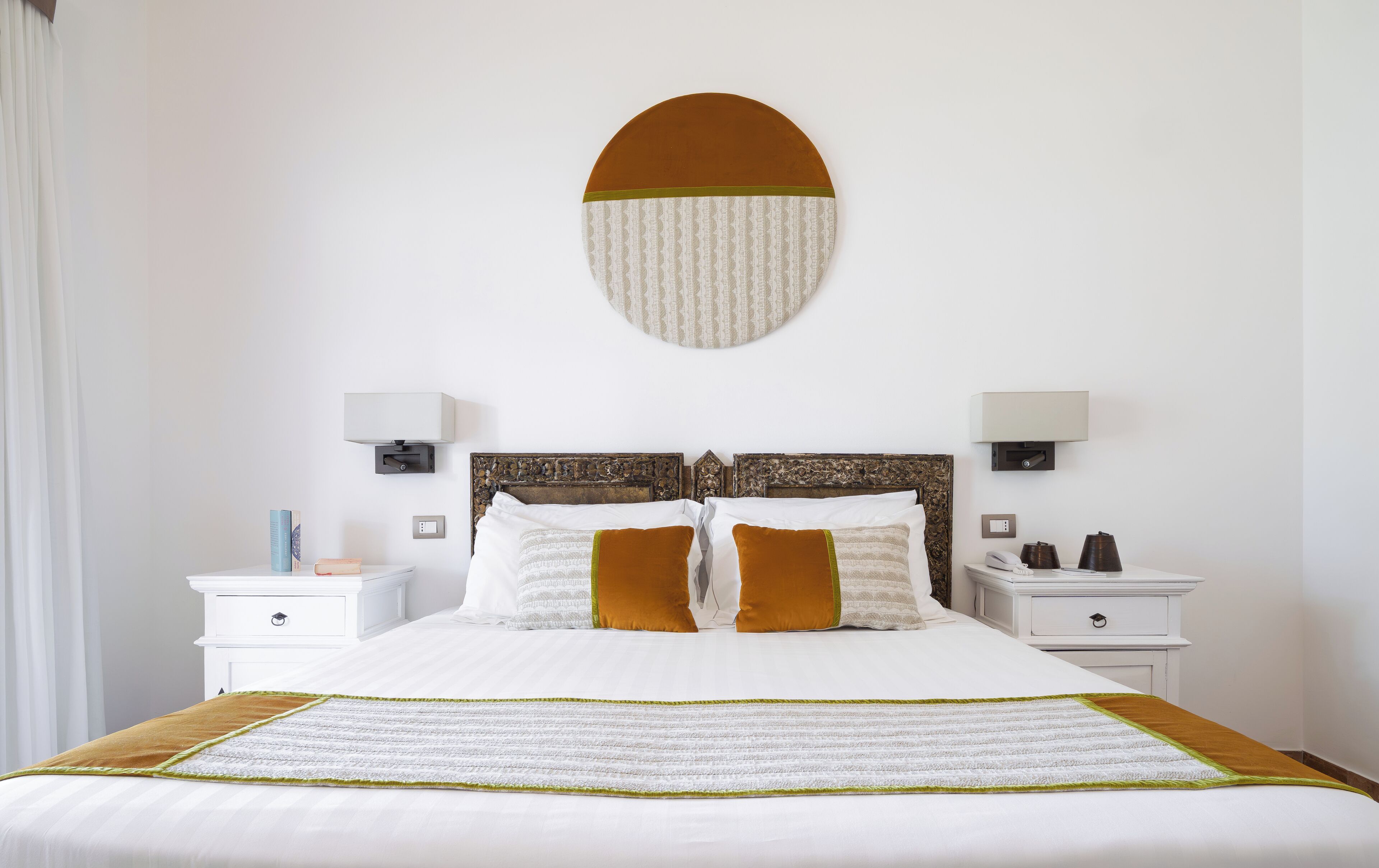 A neatly arranged hotel room with a large bed, two bedside tables with lamps, and a wall-mounted light fixture.