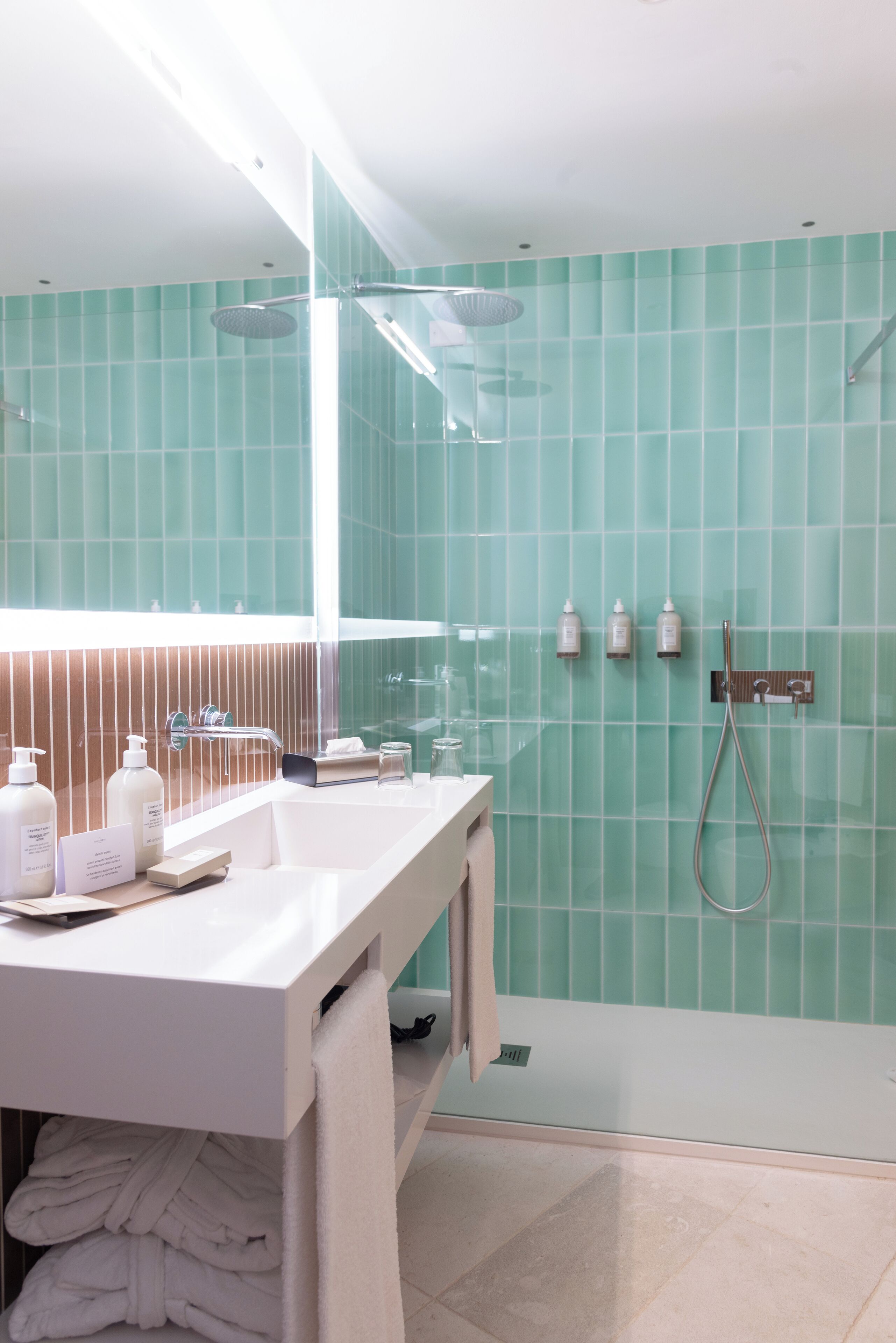Un bagno moderno con un mobile vanitario bianco, un box doccia in vetro e pareti rivestite di piastrelle verdi.
