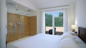 Une chambre d’hôtel avec un grand lit, un espace douche doté de portes en verre, un balcon avec une chaise et une vue sur les arbres.