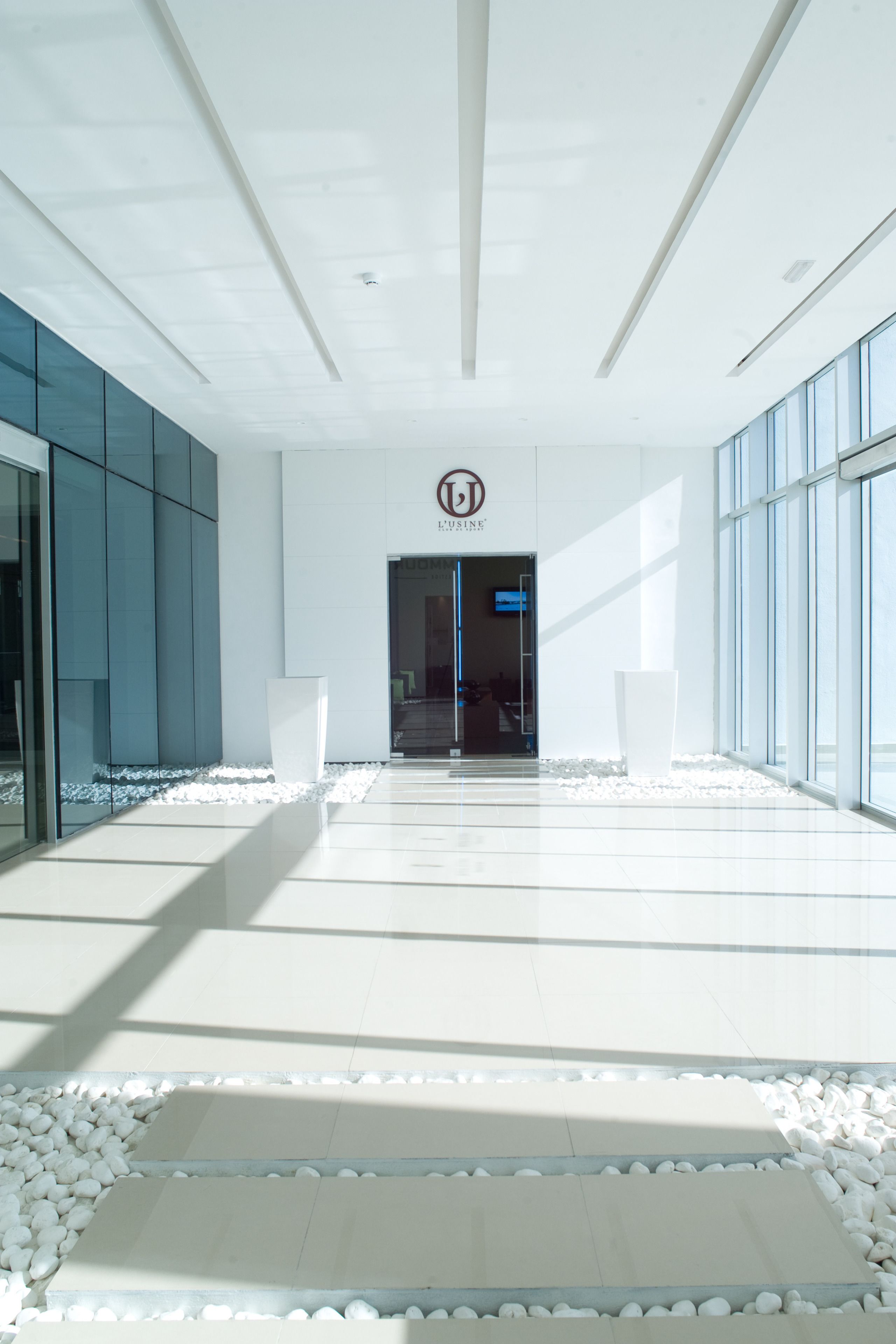 A modern hotel entrance with a glass facade, a reception desk, and a logo above the door.