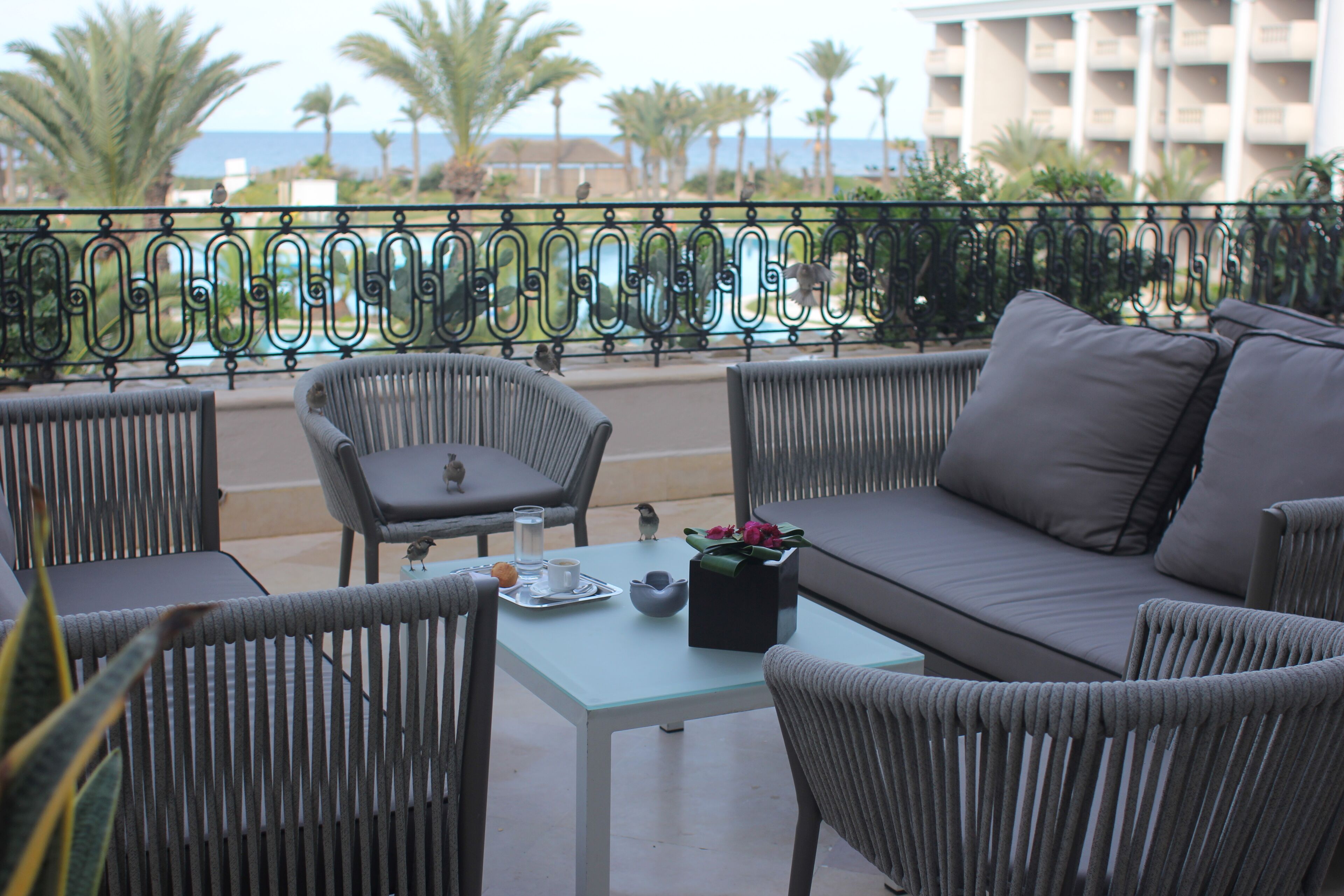 Een balkon met rieten meubels, een tafel met een dienblad en uitzicht op zee.