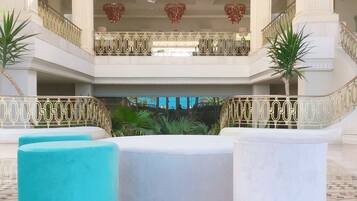 A spacious lobby with a high ceiling, a central seating area with a patterned floor, and a staircase with decorative railings.