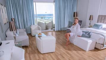 A modern hotel room with a large balcony, a sofa, a coffee table, and a bed.
