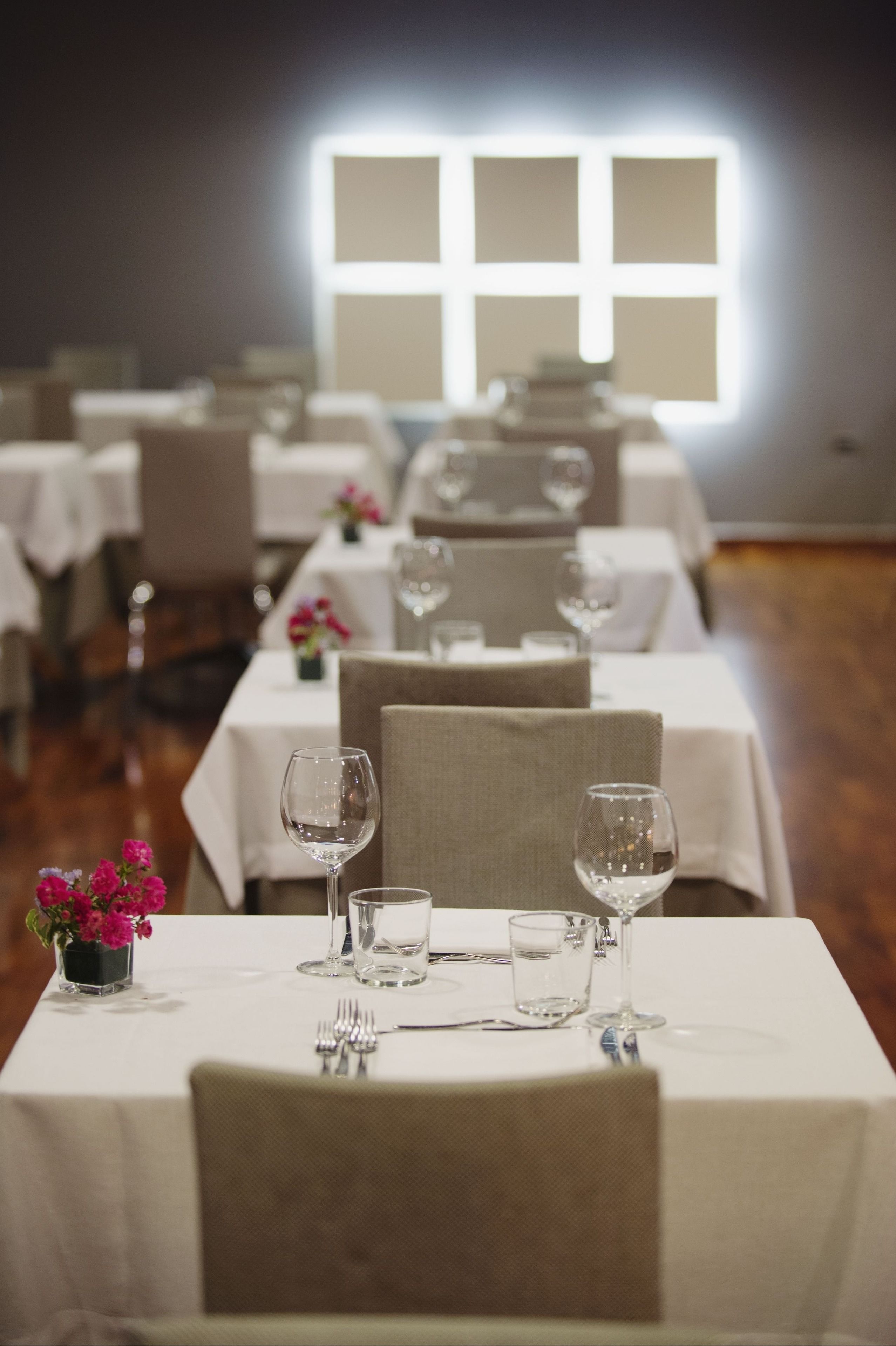 A dining area with tables set for a meal, featuring chairs, wine glasses, and a vase with flowers.