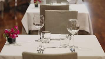 A dining area with tables set for a meal, featuring chairs, wine glasses, and a vase with flowers.