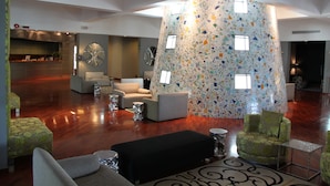 Een ruime lobby met een hoge plafond, een centraal zitgedeelte met banken en een salontafel, en een decoratieve muur met geometrische patronen.