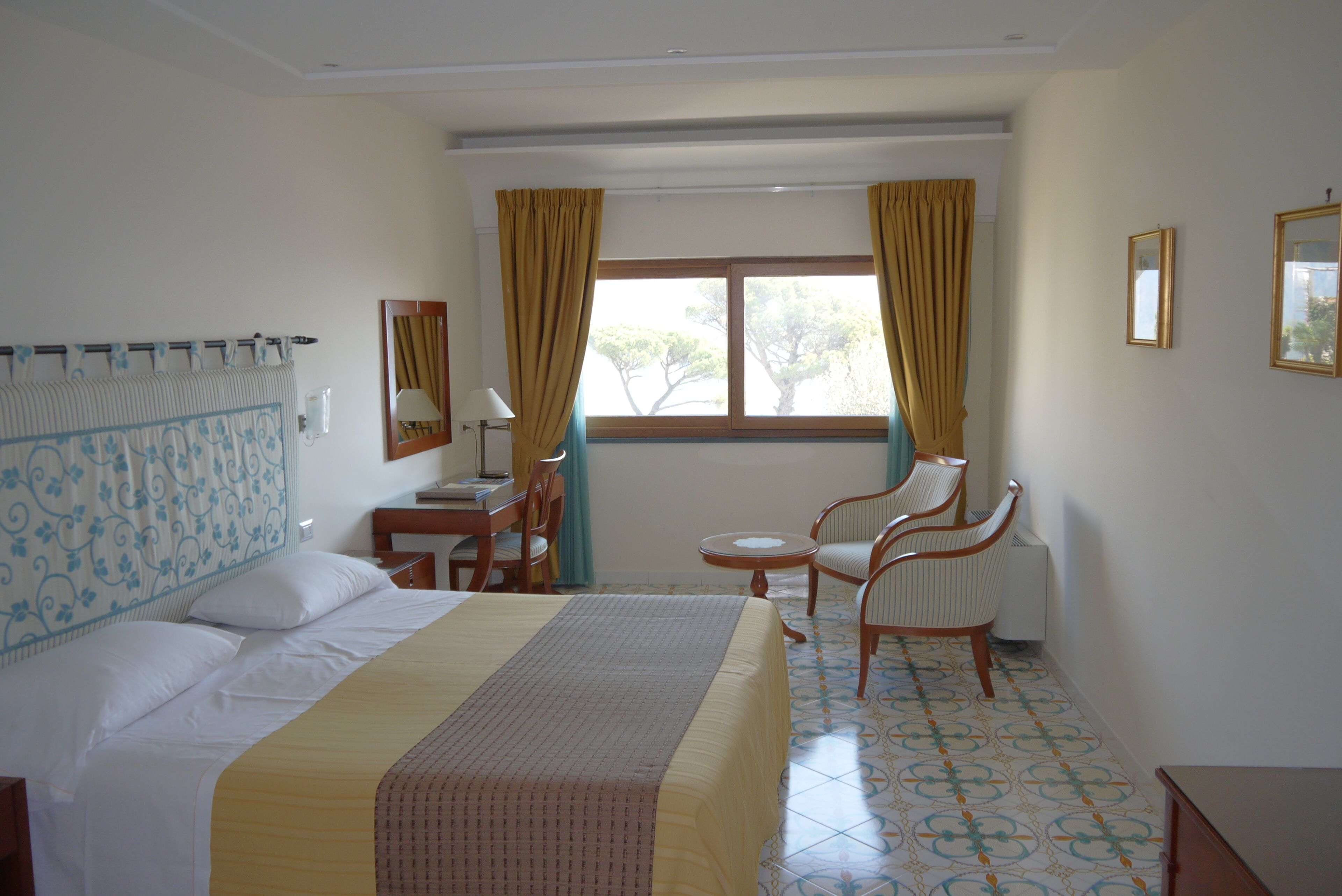 Habitación de hotel con cama, escritorio, silla y ventana con cortinas.