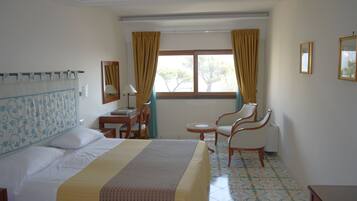Habitación de hotel con cama, escritorio, silla y ventana con cortinas.