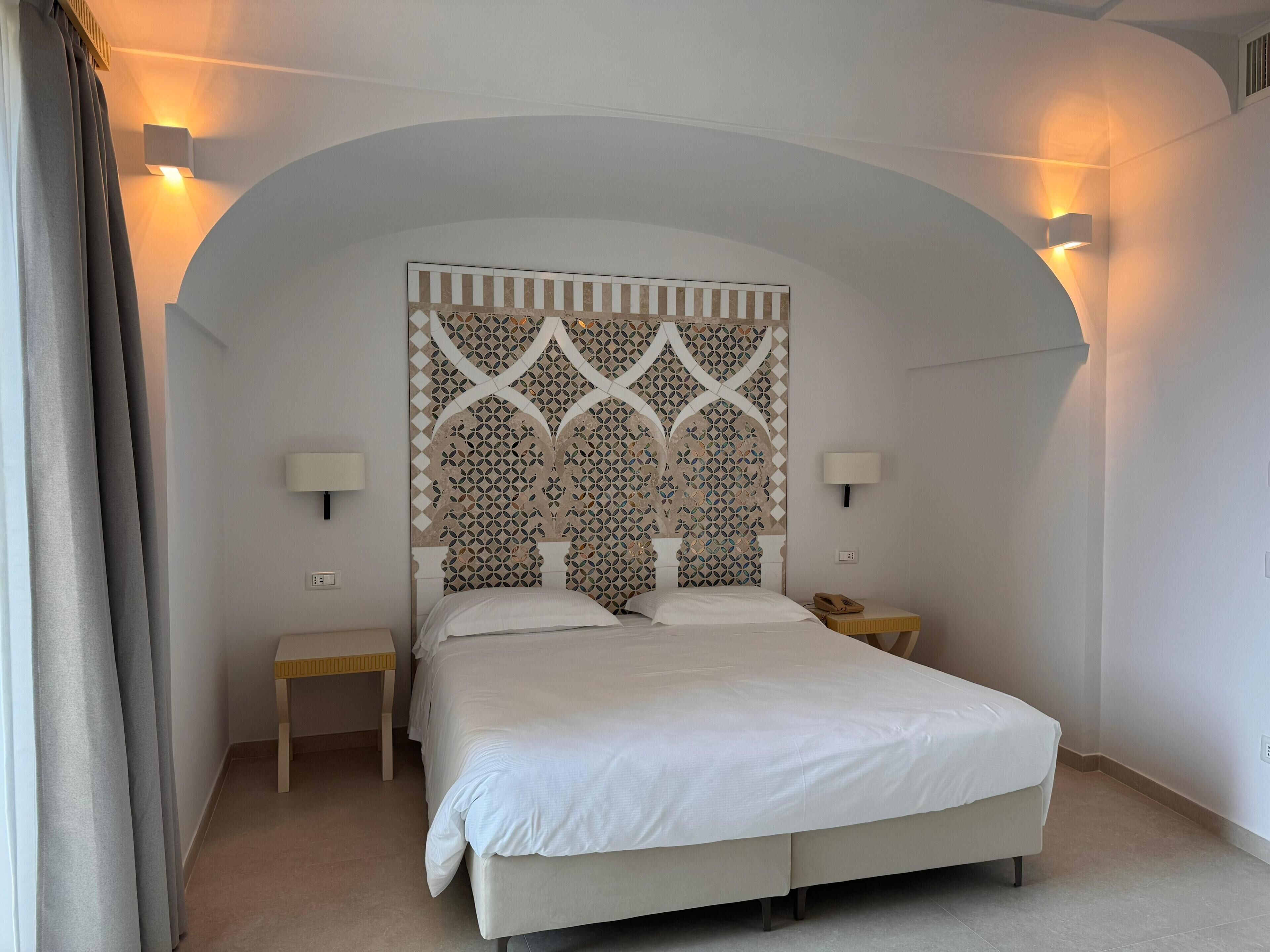 A bedroom with a bed, two bedside tables, and a decorative headboard.