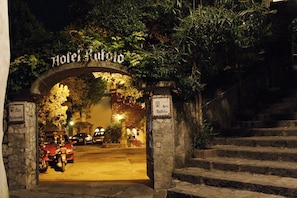 A stone archway with the sign "Hotel Rufolo" at night, leading to a building with a staircase.