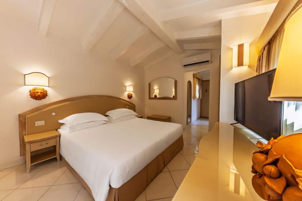 Ein Hotelzimmer mit einem großen Bett, Nachttischlampen, einem Flachbildfernseher und einem hölzernen Kopfteil.