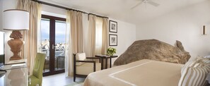 Quarto de hotel com cama, escrivaninha, cadeira, decoração com uma grande rocha e vista através de uma porta de vidro.