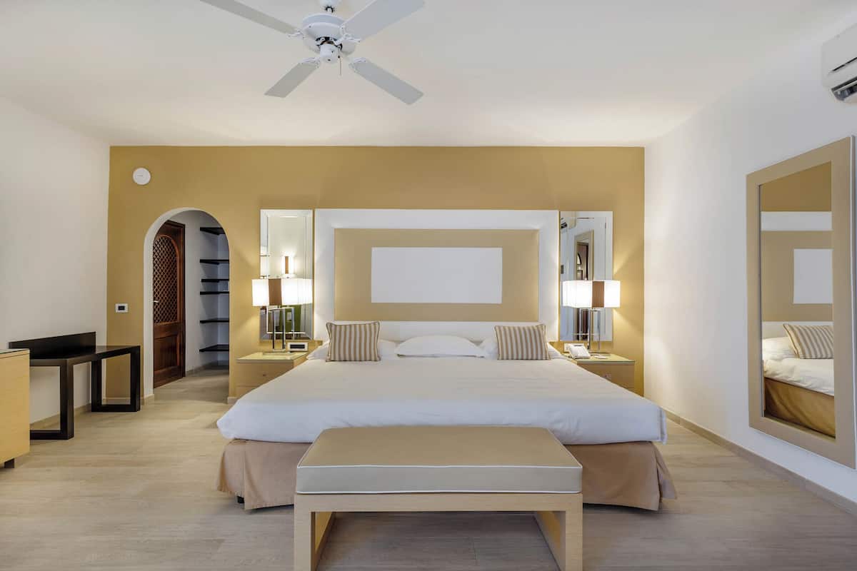 Ein Hotelzimmer mit einem großen Bett, Nachttischen mit Lampen, einem Deckenventilator und einem großen Spiegel an der Wand.