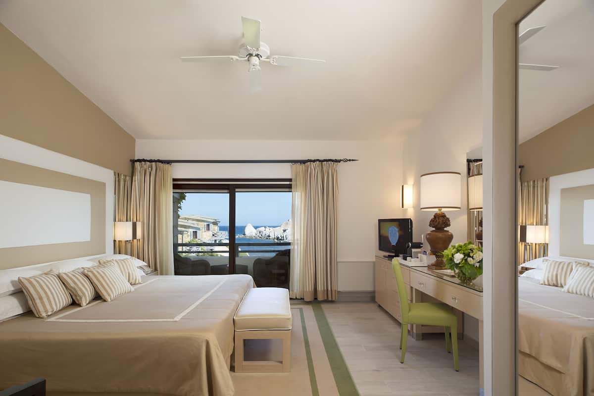 Ein Hotelzimmer mit Bett, Schreibtisch, Stuhl, Fernseher und Meerblick.