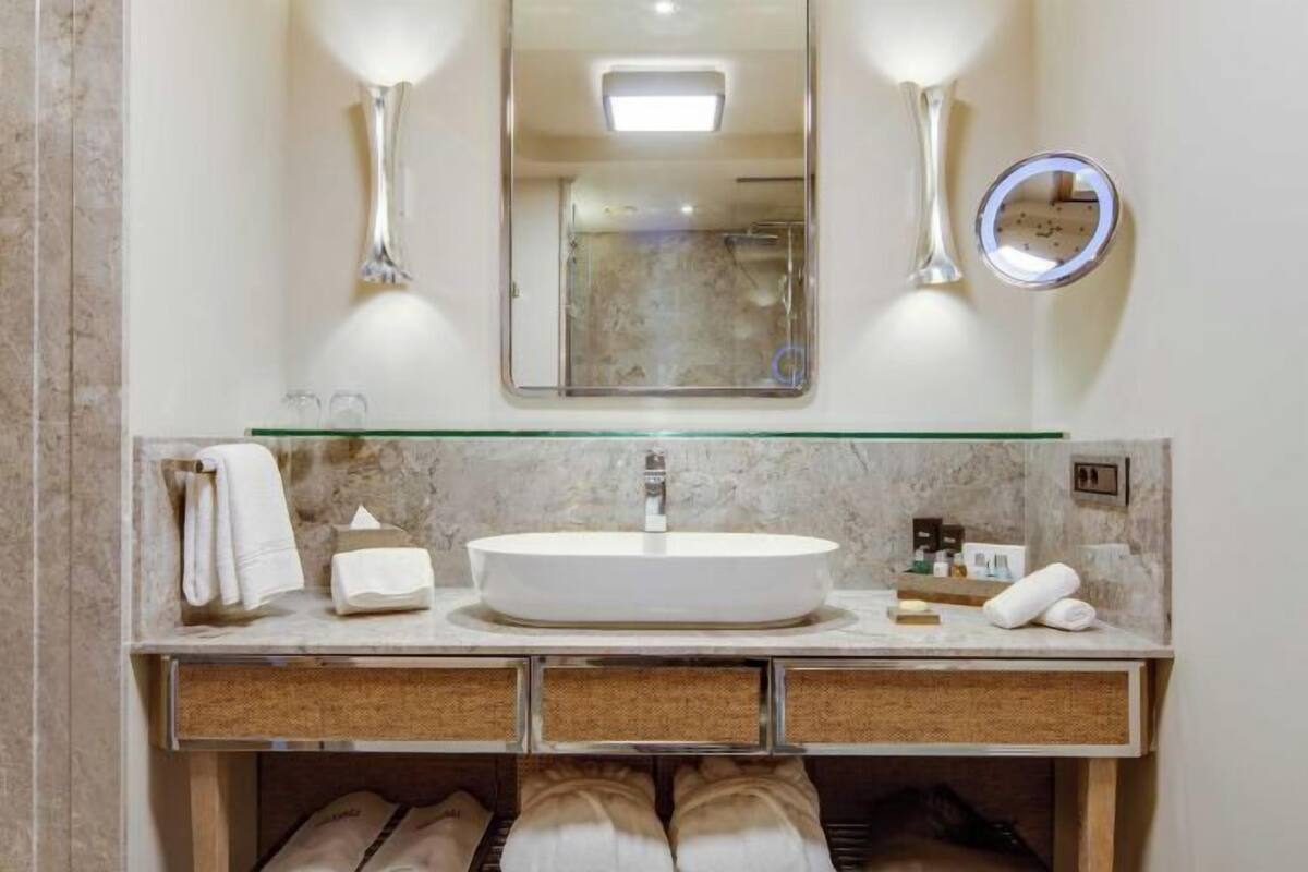 Un baño con un espejo grande, un espejo redondo, un lavabo y un perchero para toallas.