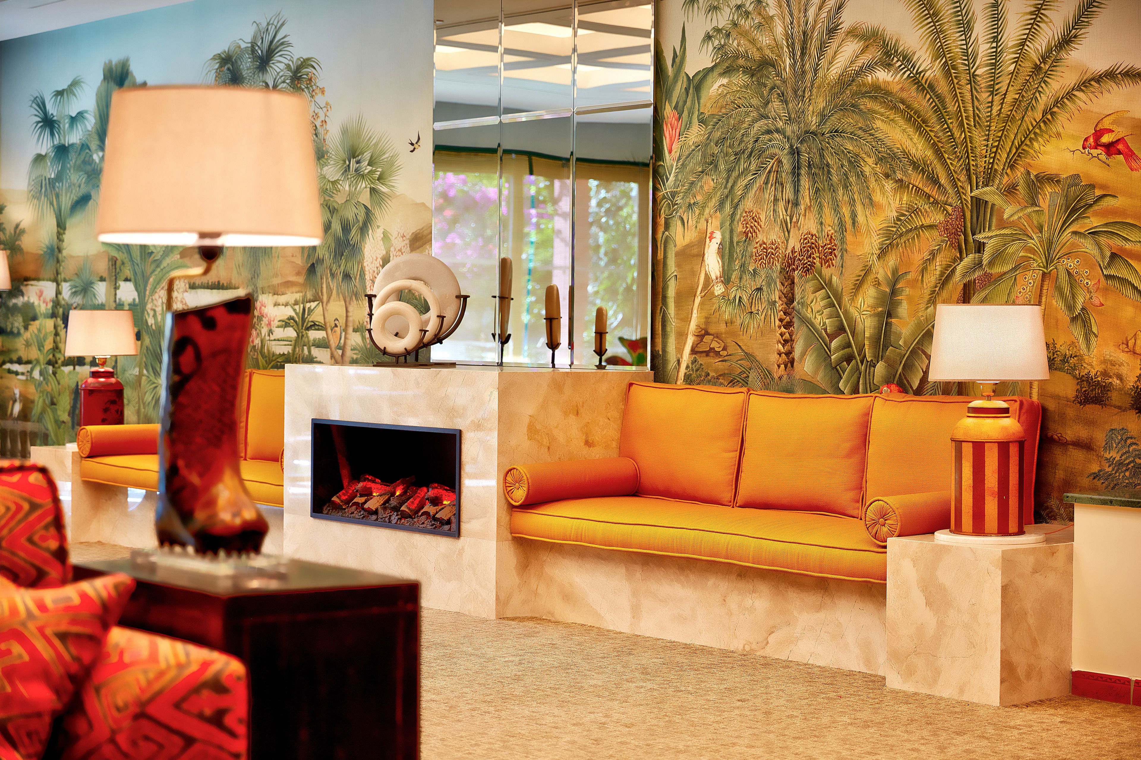 A room with a sofa, lamps, a fireplace, and a mural of tropical scenery.