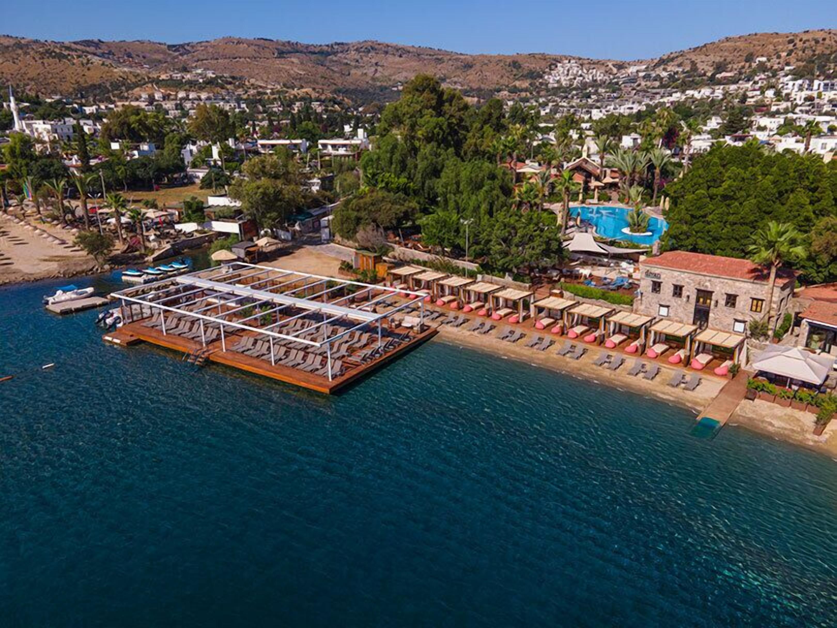 Luftaufnahme eines Küstenresorts mit einer schwimmenden Plattform, Liegestühlen und einem Poolbereich.