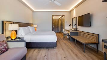 Une chambre d’hôtel moderne équipée d’un lit, de tables de chevet, d’un bureau, d’une chaise, d’un banc, d’un ventilateur de plafond et d’un téléviseur fixé au mur.