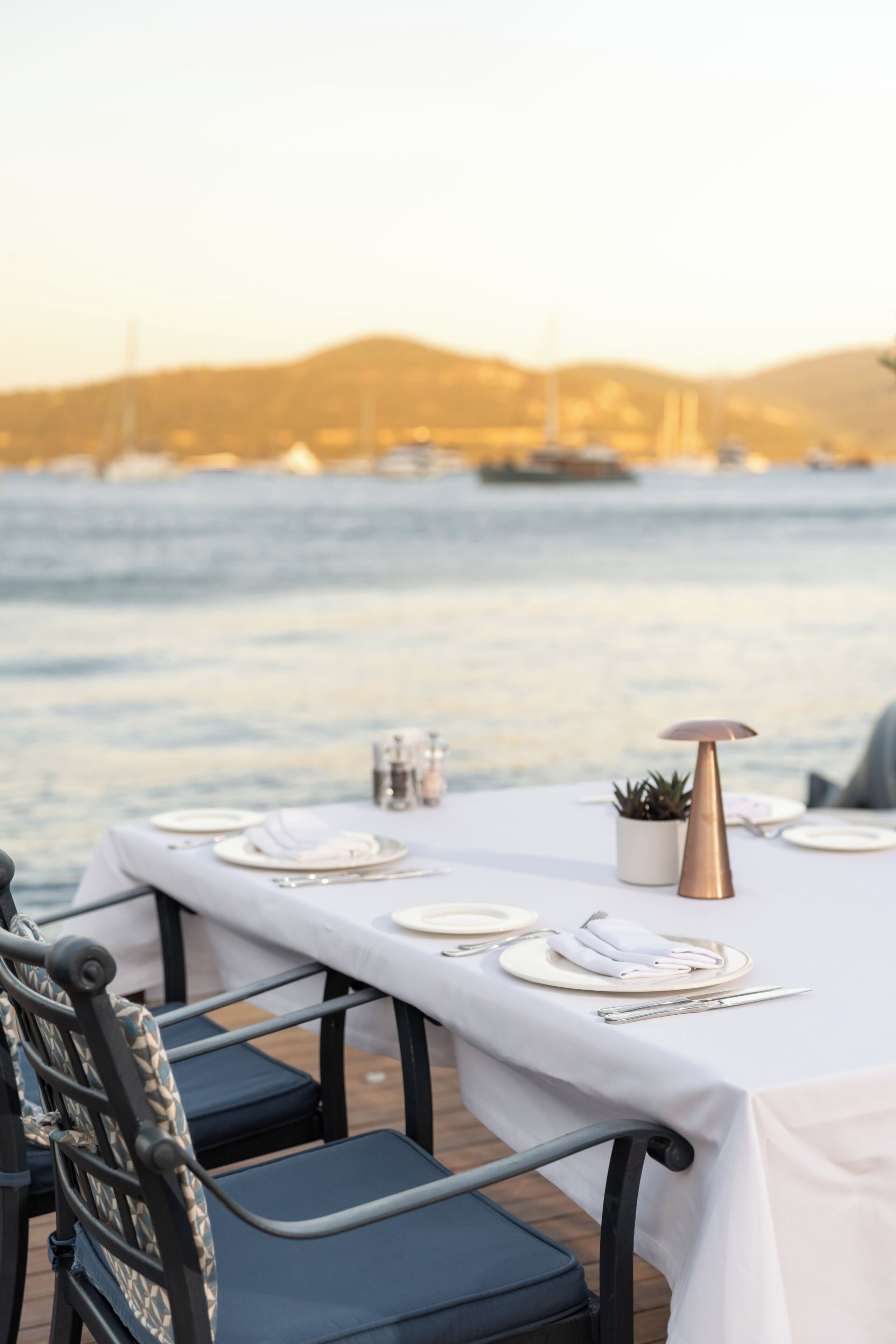 Une table dressée pour le dîner, avec une vue sur la mer et les collines en arrière-plan.