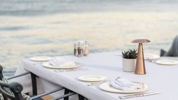 Une table dressée pour le dîner, avec une vue sur la mer et les collines en arrière-plan.
