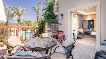 Une terrasse extérieure aménagée avec des meubles en osier, une table en verre et une vue sur une piscine et des palmiers.