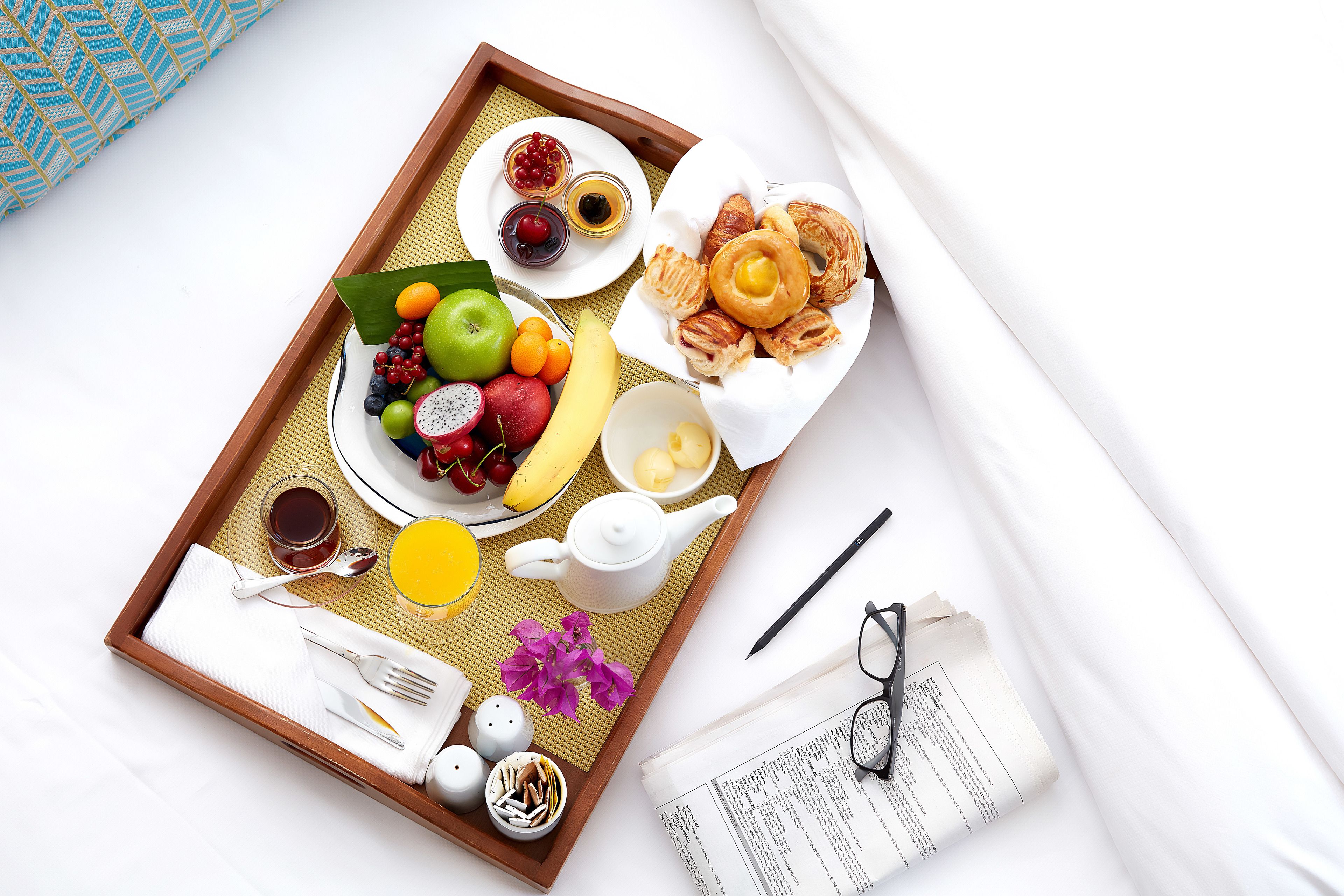 A breakfast tray with fruits, pastries, and beverages on a woven mat.
