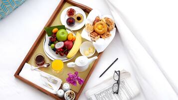 A breakfast tray with fruits, pastries, and beverages on a woven mat.