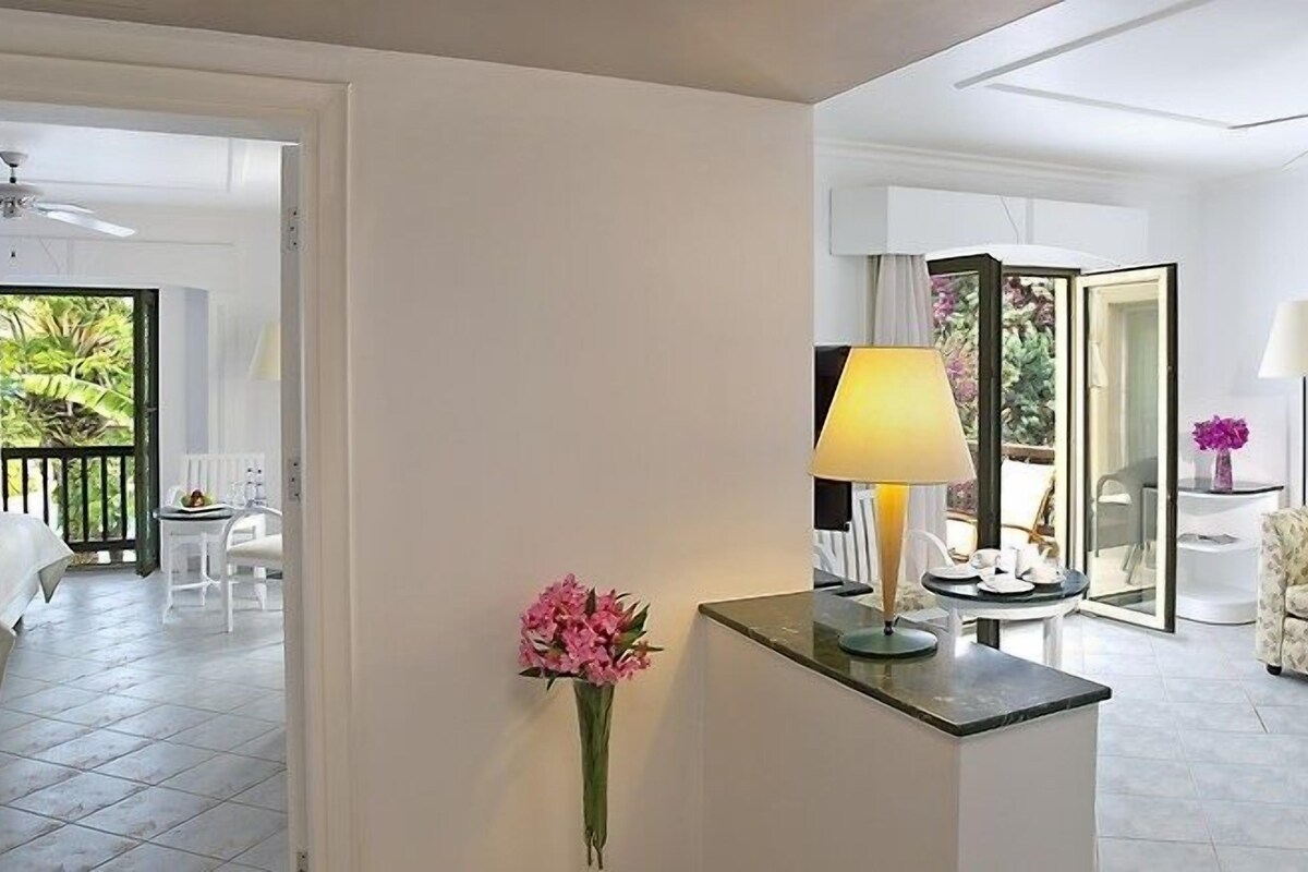 Habitación de hotel con cama, zona de estar con sofá, mesa con lámpara y vistas al exterior.