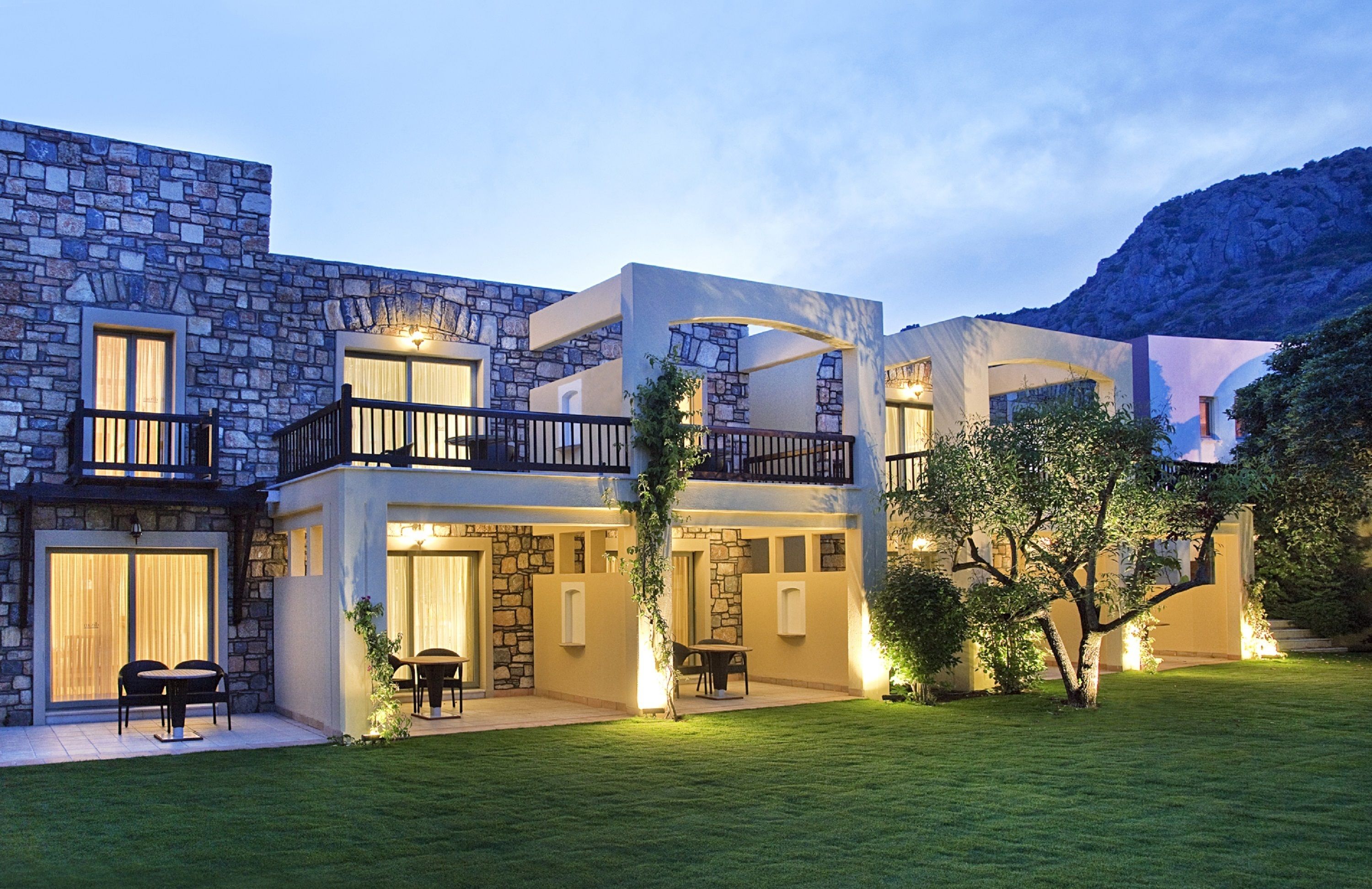 A modern two-story house with stone facade, balconies, and a well-maintained lawn.